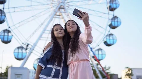 Two girls do selfie using a smartphone standing on the background of a Ferris Stock Footage 93331028
