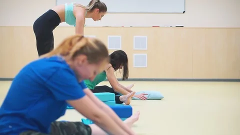 Two girls do stretching exercises sitting on blue mats. Fitness trainer helps Video stock 102534835