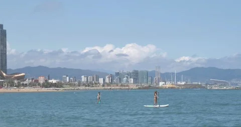 Two girls doing paddle surf in the Barcelona sea with the Barcelona skyline Stock Footage 133260320