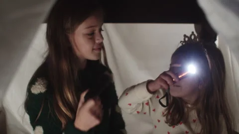 Two girls enjoying flashlight fun under bedsheets at home in the evening Stock Footage 320031035
