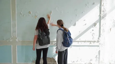 Two girls explore abandoned building with peeling plaster walls Stock Footage 342087598