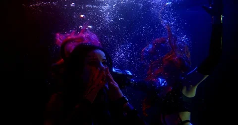 Two girls float in the dark under the water. the brunette moves her hands in Stockbeeldmateriaal 124053012
