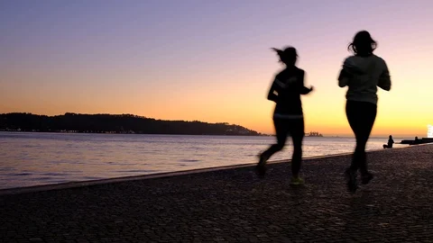 Two girls jogging next to a river Tejo in sunset Stock Footage 129279064