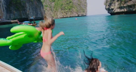 Two girls jumping off authentic long tail boat into clear blue ocean water in Th Stock Footage 201096803