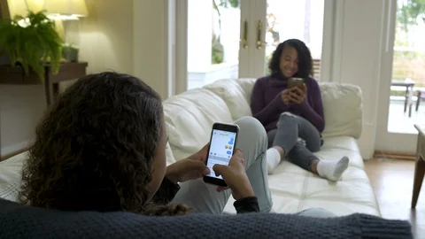 Two girls laying on sofa using their mobile phones. 動画素材 88174672