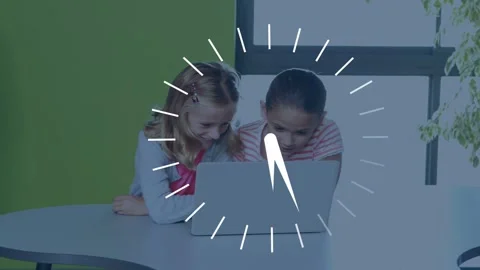 Two girls leaning at table tapping laptop activating spinning clock for school Stock Footage 335651728