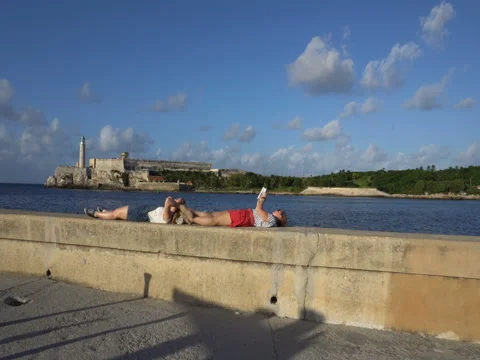 Two girls lie on the seafront, read a book and relax at sunset Stock Footage 70991699
