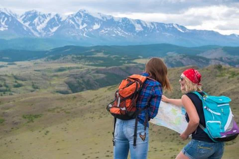 Two girls look at the map on the background of mountains and thi Stock Photos