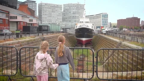 Two girls looking at a large ship in a dry dock at Liverpools waterfront Stock-Footage 327458123