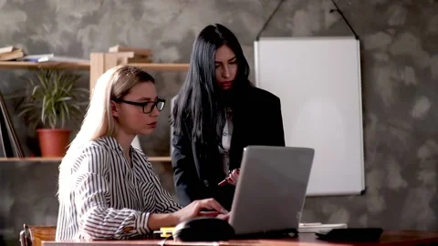 Two girls in the office check data on a laptop using a digital tablet. Company Stock Footage 131534245