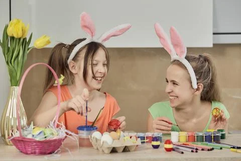 Two girls paint Easter eggs with colorful paint in the kitchen and laugh. Foto stock