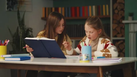 Two girls prepare for school test together, reading and taking notes at home Stock Footage 343423470