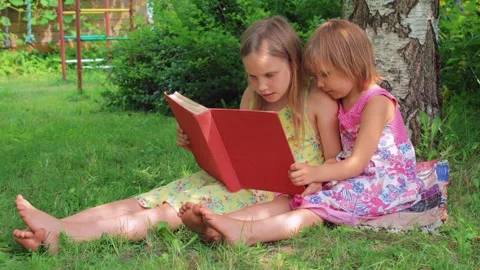 Two girls reading red book together in a sunny backyard garden Video stock 294596643