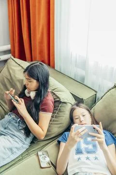 Two girls relaxing on sofa using smartphone, headphones, casual home setting Stock Photos