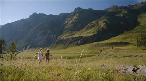 Two girls run in a meadow on the background of mountains Stock Footage 40452875