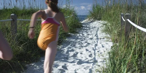 Two girls running on the sandy path towards the sea, medium shot Stock Footage 103486719