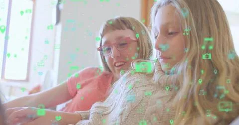 Two girls scrolling device on sofa in living room, with floating green digital Stock Photos