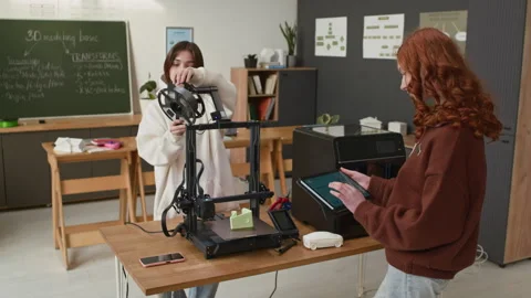 Two Girls Setting Up 3D Printer Via Tablet in Modern School Classroom Stockbeeldmateriaal 335696553