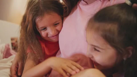 Two girls share a moment of laughter while sitting close to an adult in a cozy Stock Footage 330750102