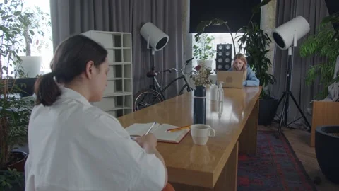 Two girls sit at long table opposite sides, workspace in restaurant, observe a Stock Footage 132671278