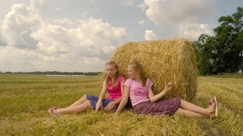 Two girls sit near a stack of straw and talking. Video stock 52461254