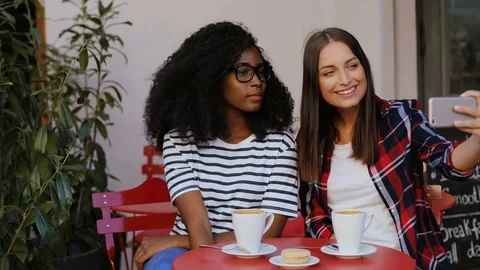 Two girls sitting at table in cafe, taking selfie and showing peace sign Stock Footage 81834430