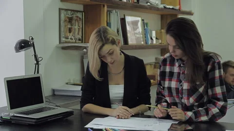 Two girls at a table considering blueprints, a young man comes to them and takes Stock Footage 62759450