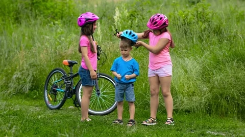 Two girls try to put a protective bicycle helmet on their little brother Stock Footage 148552227