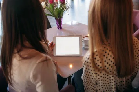 Two girls use a tablet while sitting in a cafe and drinking coffee. Business Stock Photos