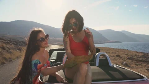 Two girls using map, sitting on a trunk of cabrio. Best friends spend summer Stock Footage 181170258