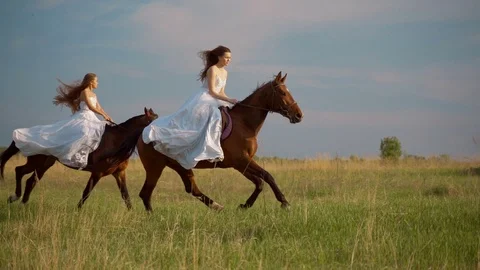 Two girls in white dresses on horseback. Girls jumping on the field on horseback Stock Footage 108397553