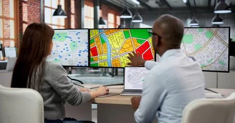 Two GIS Analysts In Office Using Computers To Review Urban Planning Maps. The Foto stock