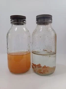 Two glass bottles showcasing different colored liquids with sediment at the b Foto stock