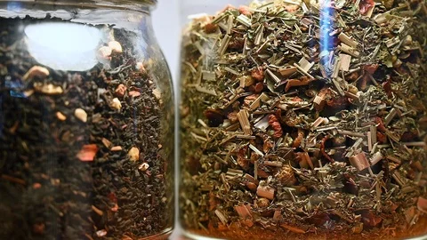 Two glass jars full of herbs and a hand with a tea inox diffuser Stock Footage 105134679