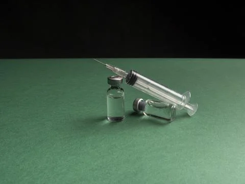 Two glass vials in which a liquid with a vaccine stand a syringe lies next to Stock Photos