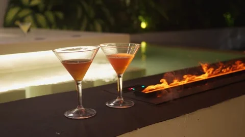 Two glasses of alcohol sit on bar deep rich colors enhanced by glowing fire Stock Footage 312506329