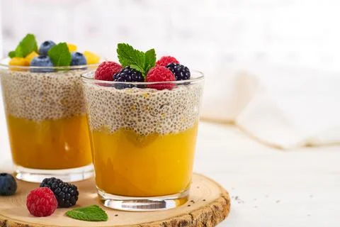 Two glasses of chia pudding with mango puree and berries on light background Stock Photos