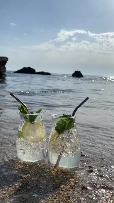 Two glasses with a cocktail with lemon and a mint leaf on the seashore Stock Footage 280709336