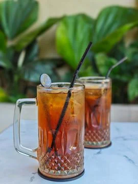Two Glasses of Cold Iced Tea Served Outdoors with Black Straws Stock Photos