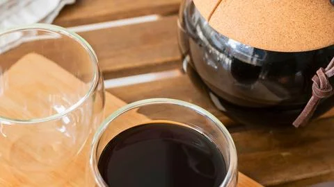 Two glasses of drinks and a coffee pot on a wooden table Stock Photos