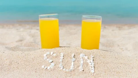 Two glasses filled with juice on sandy beach, against the background of the sea Stock Footage 79476486