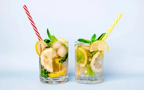 Two glasses of lemon mint water with straws on blue background Stock Photos
