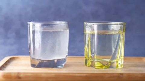 Two glasses of liquid one clear and one yellow on wooden tray with dark bac.. Stock Footage 333260430