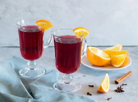 Two glasses of mulled wine, oranges, spices, light background, gray textiles Stock Photos