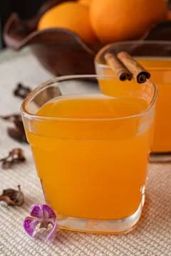 Two glasses of orange juice with two cinnamon sticks and a brown ceramic basket Stock Photos