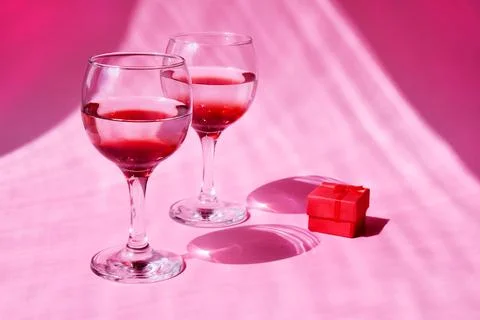 Two glasses with a red gift box on a pink background with sun glare and hard  Stock Photos