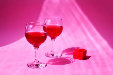 Two glasses with a red gift box on a pink background with sun glare and hard  Stock Photos