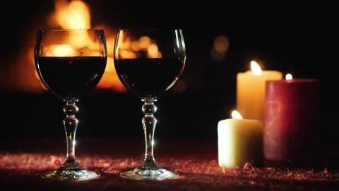 Two glasses of red wine and flickering candles create romantic ambiance wit.. Видео 334993137