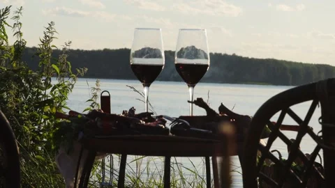 Two glasses of red wine at picnic by river, romantic outdoor lifestyle Video stock 332307608