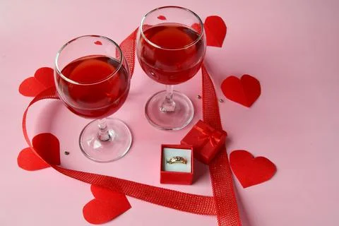 Two glasses of red wine with a ring in a red gift box with red hearts and a r Stock Photos